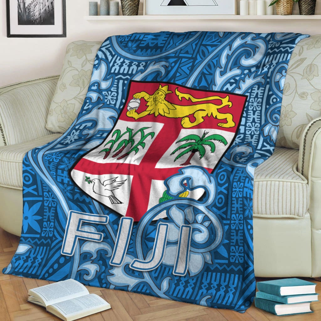 Blue tapa pattern blanket with Fiji crest and FIJI letters, folded on couch