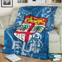 Blue tapa pattern blanket with Fiji crest and FIJI letters, folded on couch