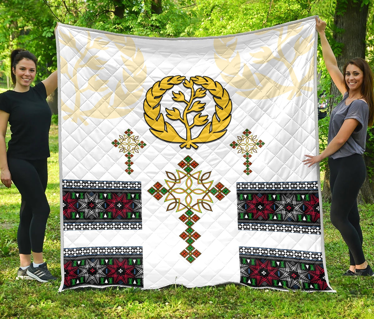 White quilt laid out outdoors, diamond quilting with gold tree and Eritrean cross motif