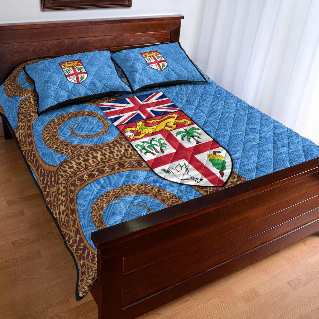 Blue Fiji Day quilt on bed with two pillows; circular motifs, shields, and “FIJI DAY” text