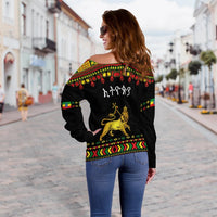 Back view: black off-shoulder sweater with lion graphic and rainbow Ethiopian border, long sleeves