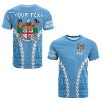 Camiseta azul con escudo Fiji y patrón geométrico en V, manga con franja blanca