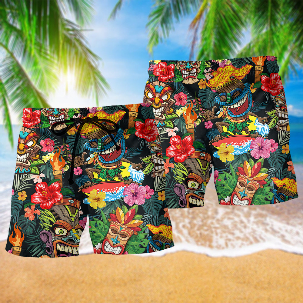 Two pairs black Hawaiian shorts with tiki mask print and red hibiscus flowers