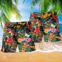 Two pairs black Hawaiian shorts with tiki mask print and red hibiscus flowers