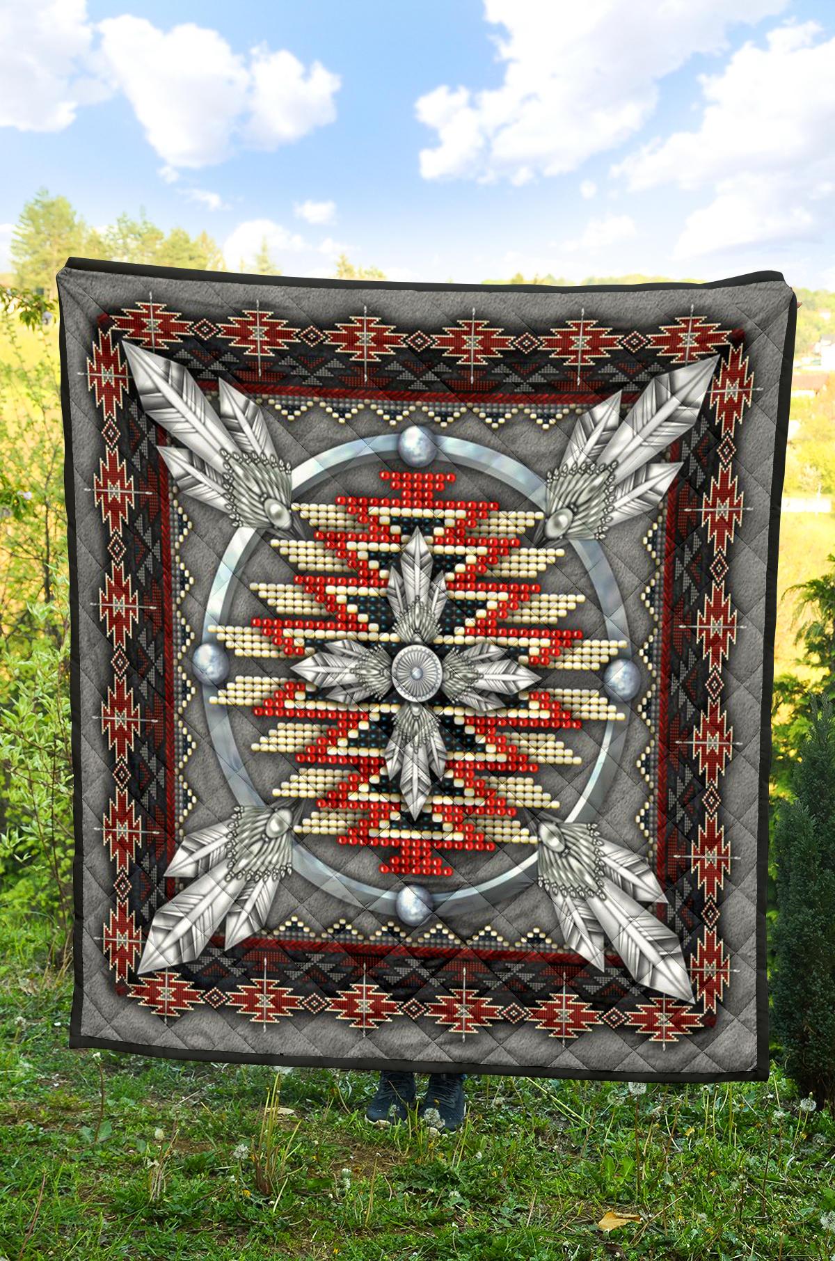 Grey quilt featuring a central feathered figure in red/white beads with a black geometric frame.