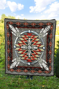 Grey quilt featuring a central feathered figure in red/white beads with a black geometric frame.