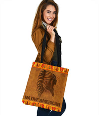 Brown Native American tote with headdress face graphic, orange pattern top band, black straps