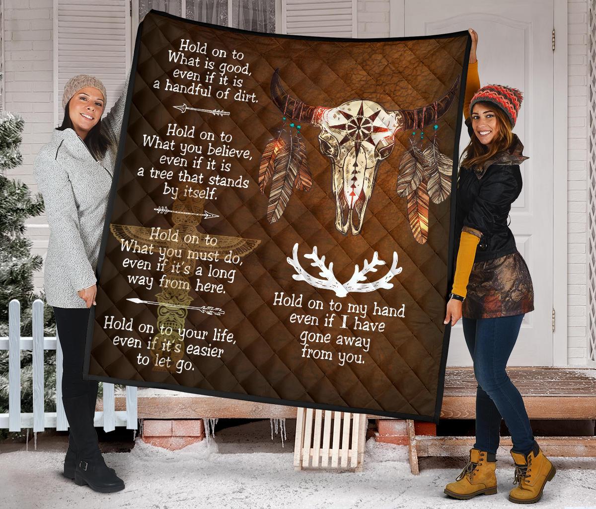 Brown quilt featuring centered bison skull, dreamcatcher-style feathers, and white text