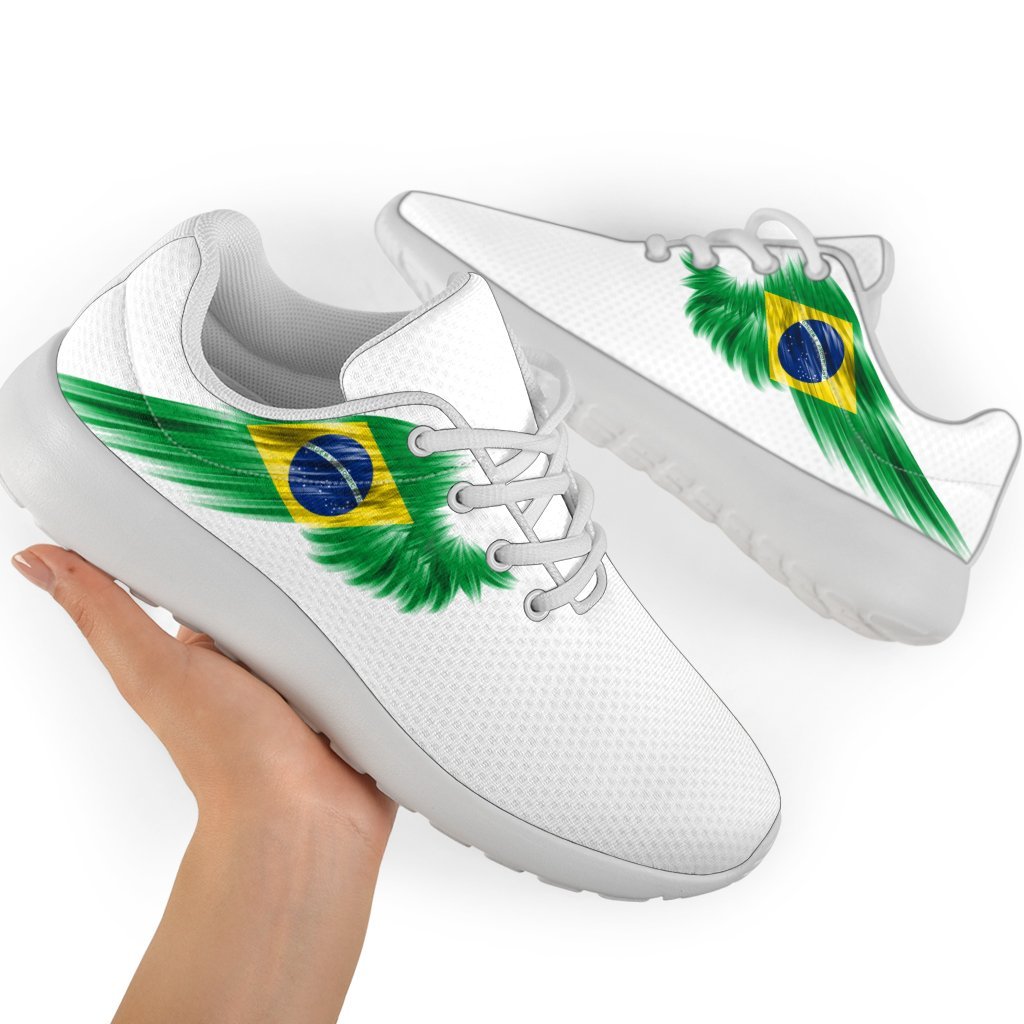 White sneakers with Brazil flag wing graphic and green laces, hand holding pair