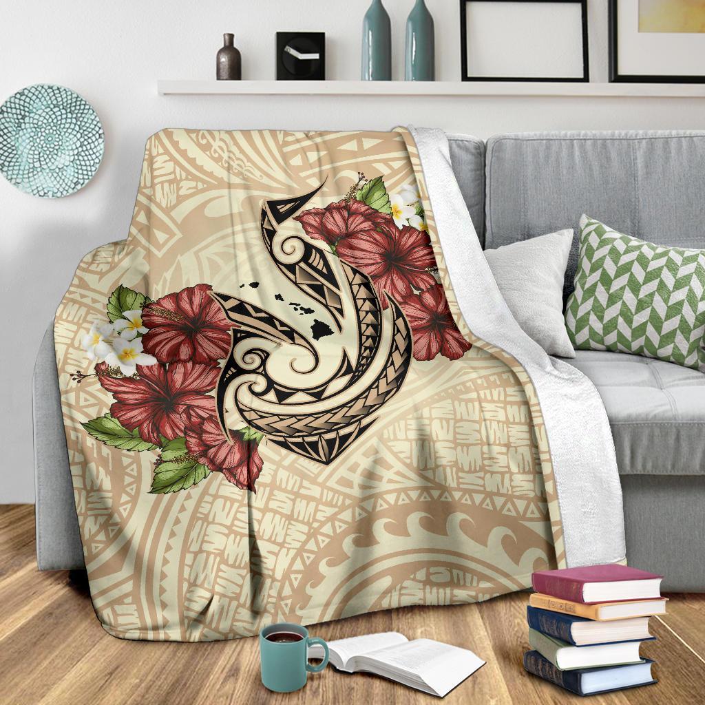 Beige blanket with large fish hook emblem and red hibiscus blooms over tribal print