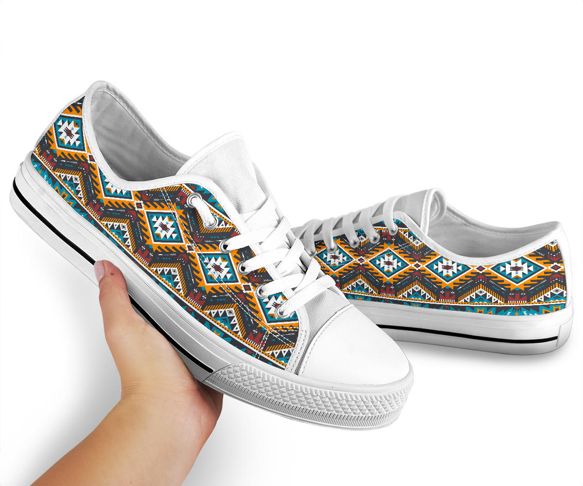 Single sneaker held by hand; white low top with multicolor Aztec geometric upper