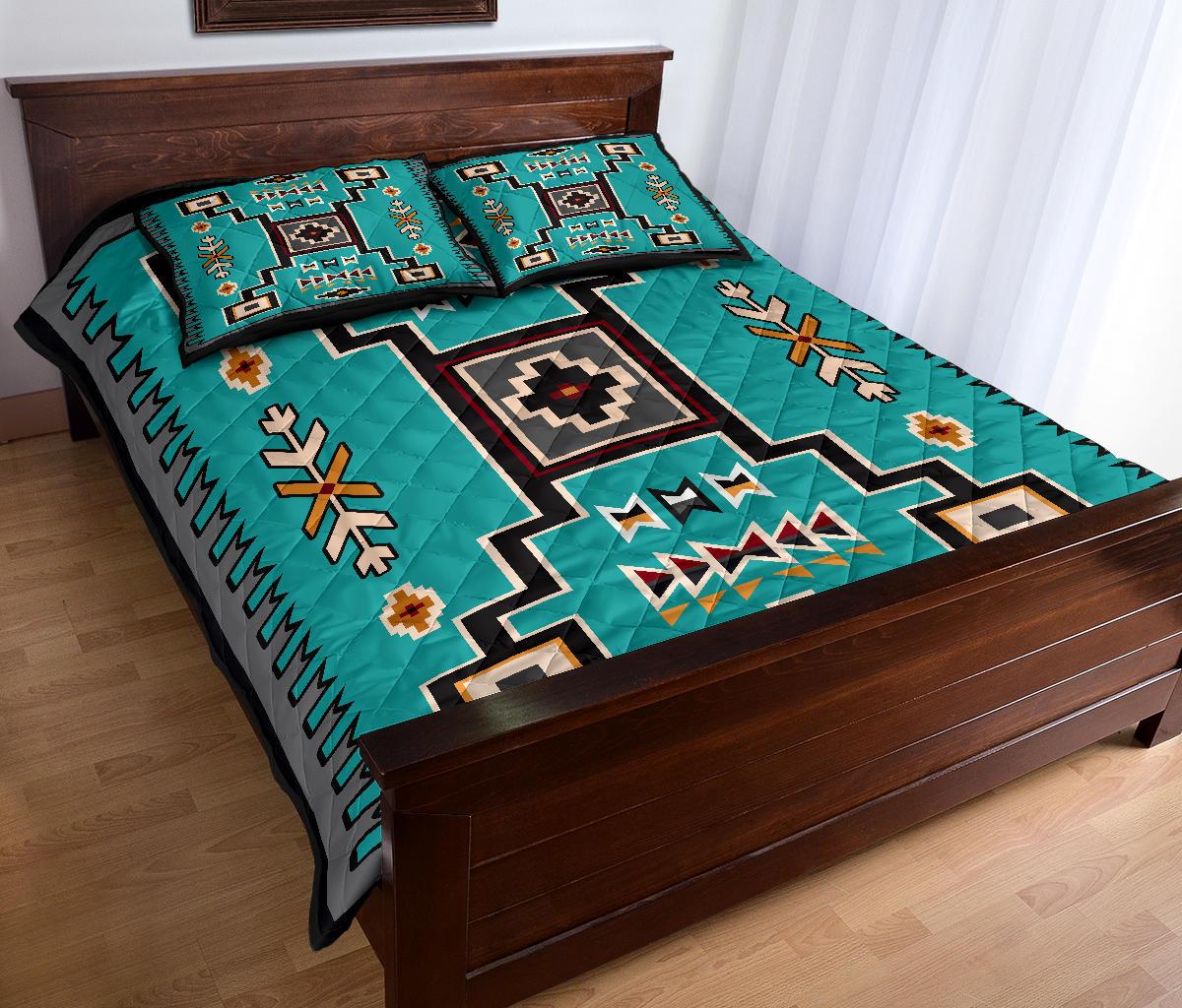 Teal quilt and two pillowcases featuring Native-inspired patterns, zigzag bands, and floral motifs