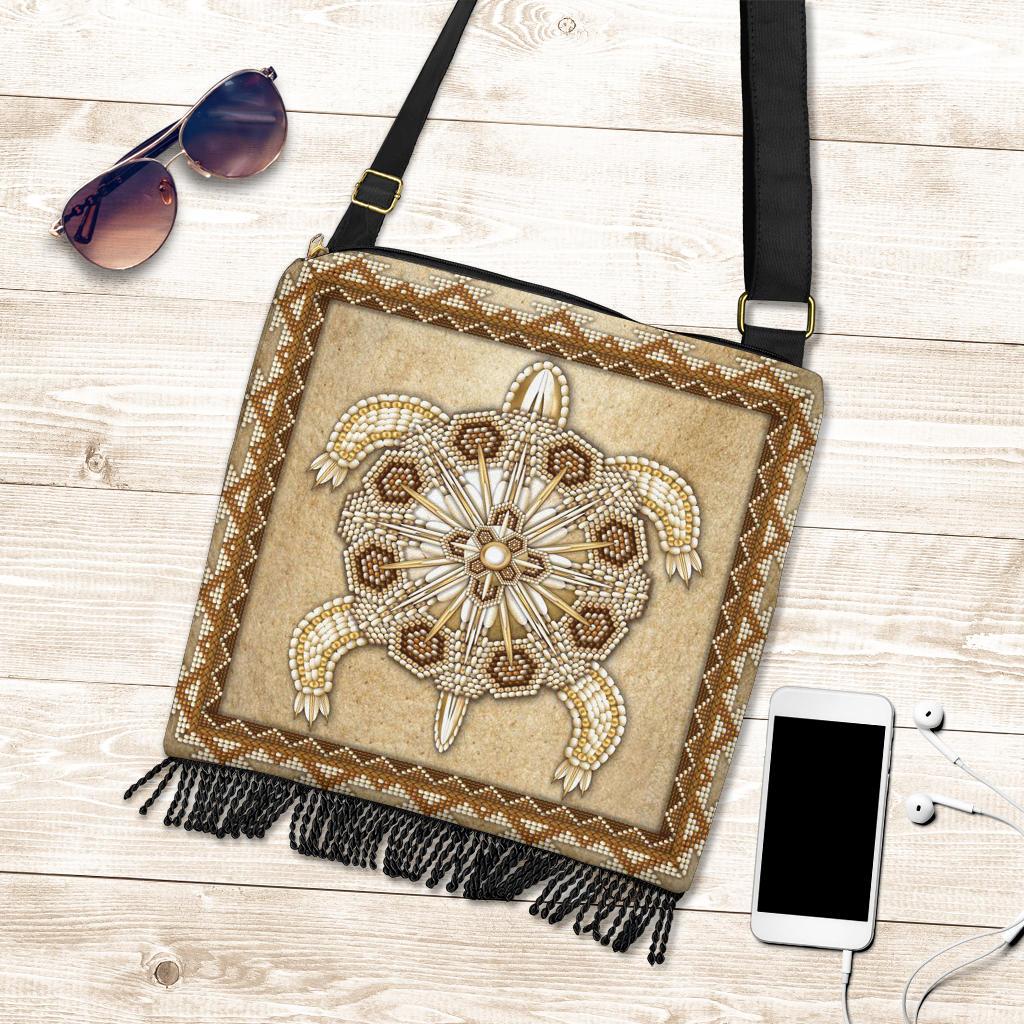 Beaded tan crossbody handbag with floral/star beadwork and fringe trim; smartphone for scale