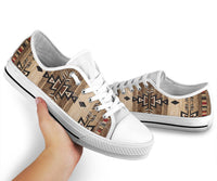 Low-top sneakers with beige arrow print and white toe caps, shown in hand