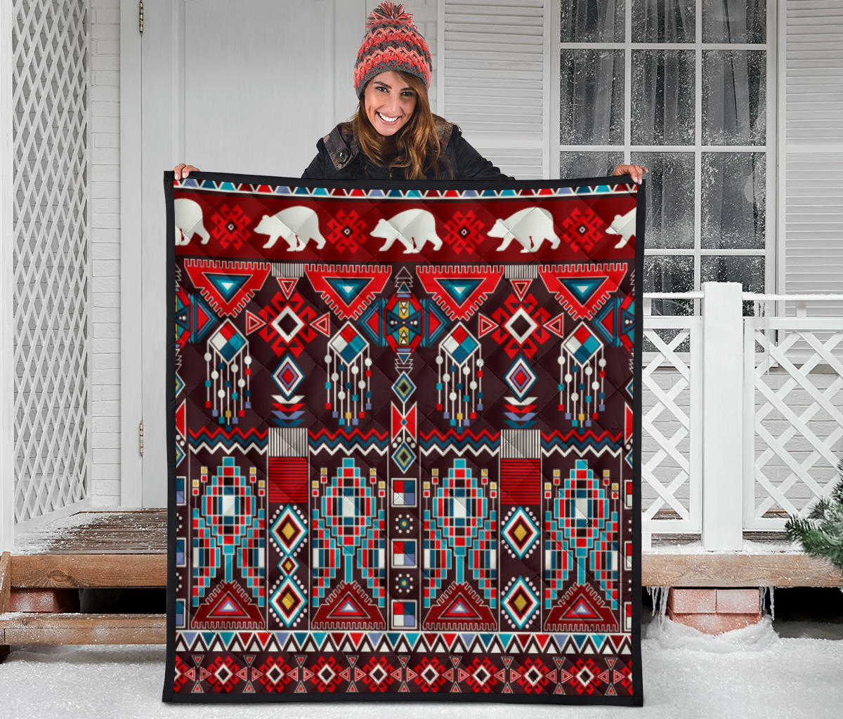 Quilt on porch rail: white bear figures, red and teal geometric blocks with dangling beaded lines