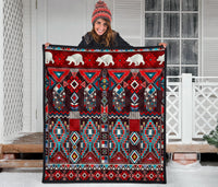 Quilt on porch rail: white bear figures, red and teal geometric blocks with dangling beaded lines