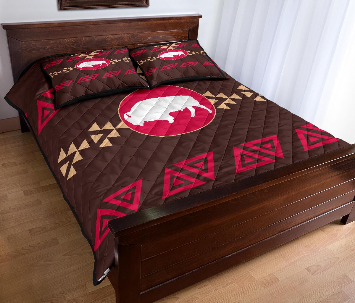 Brown quilt with pink bison oval centerpiece and red triangle motifs, two decorative shams