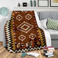 Brown geometric throw blanket draped over a seat, featuring diamond shapes and zigzag trim