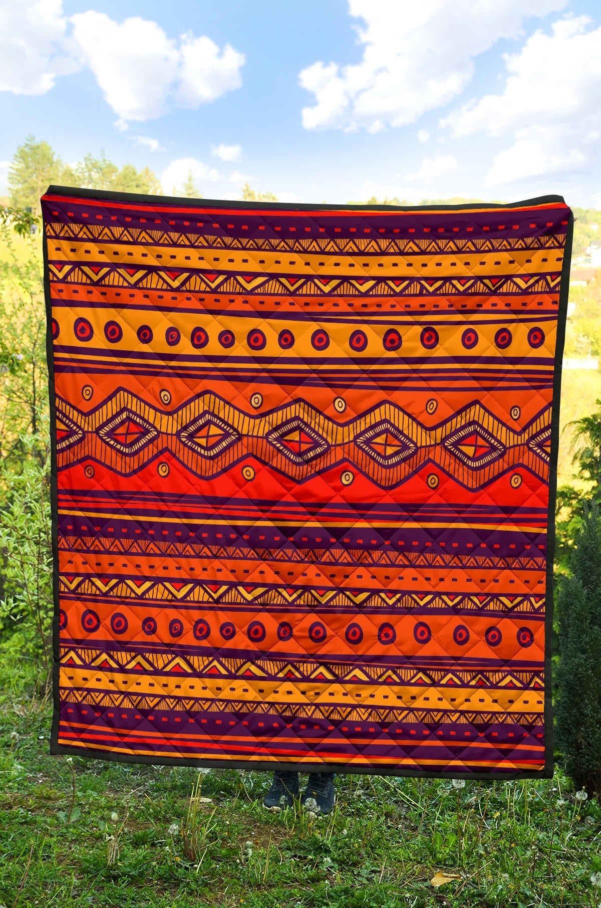 Orange quilt laid flat outdoors with navy, black, and yellow geometric stripes and diamond shapes