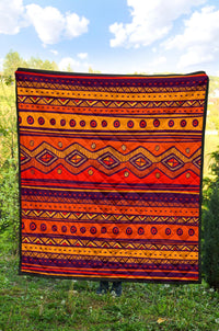 Orange quilt laid flat outdoors with navy, black, and yellow geometric stripes and diamond shapes