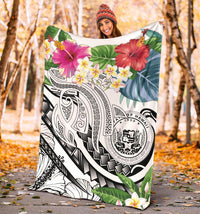White Polynesian blanket held outdoors with plumeria blossoms, tropical leaves, and tribal emblem