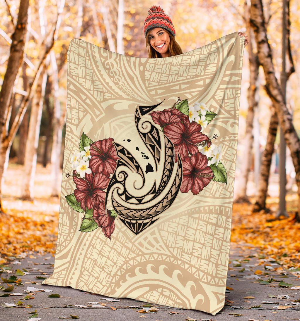 Beige Polynesian blanket outdoors showing fish hook motif and red hibiscus plumeria flowers