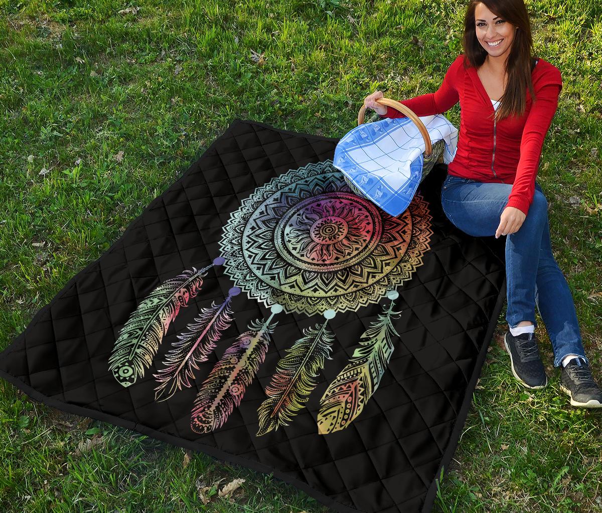 Black quilt with multicolor dreamcatcher mandala and colorful feather print, draped over grass