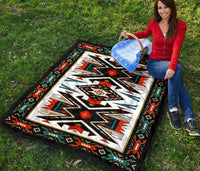 Native American-style quilt laid on grass, black border with red, green, teal, and white design