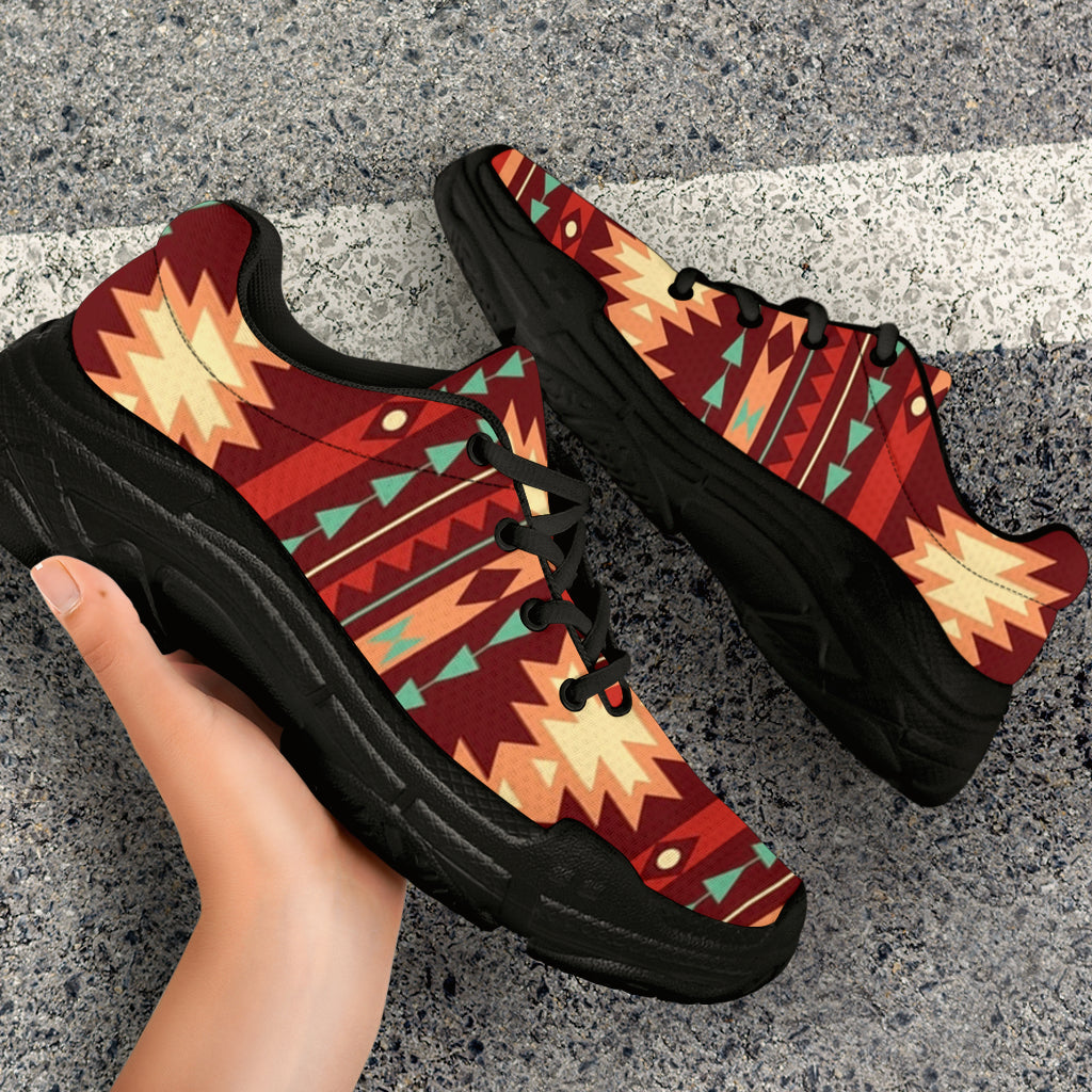 Red Native-inspired pattern chunky sneakers angled on pavement, black sole