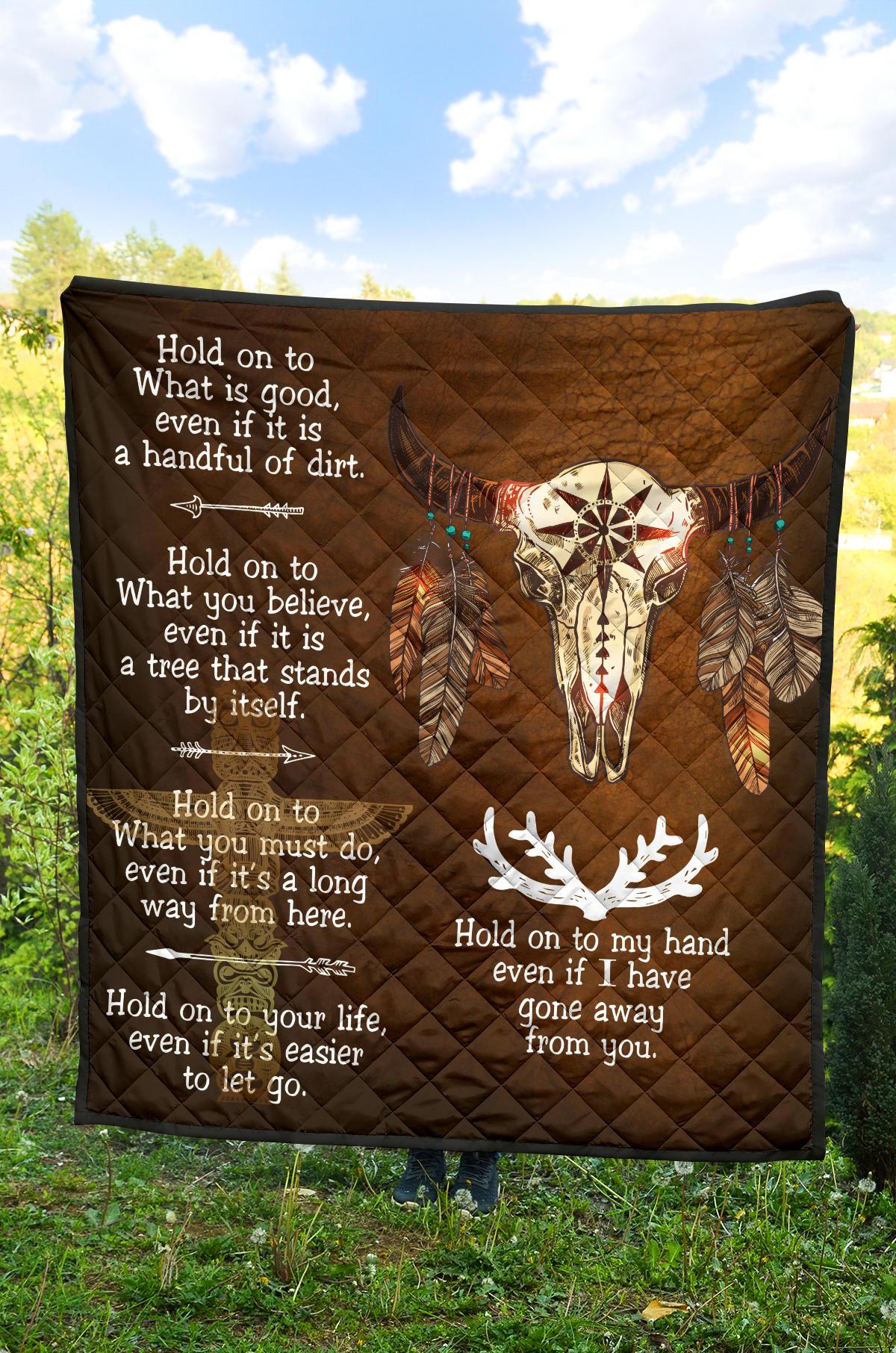 Brown quilt laid on grass showing bison head artwork and white decorative phrases