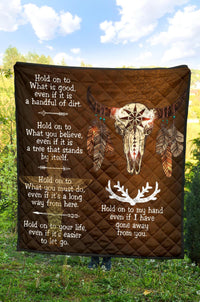 Brown quilt laid on grass showing bison head artwork and white decorative phrases