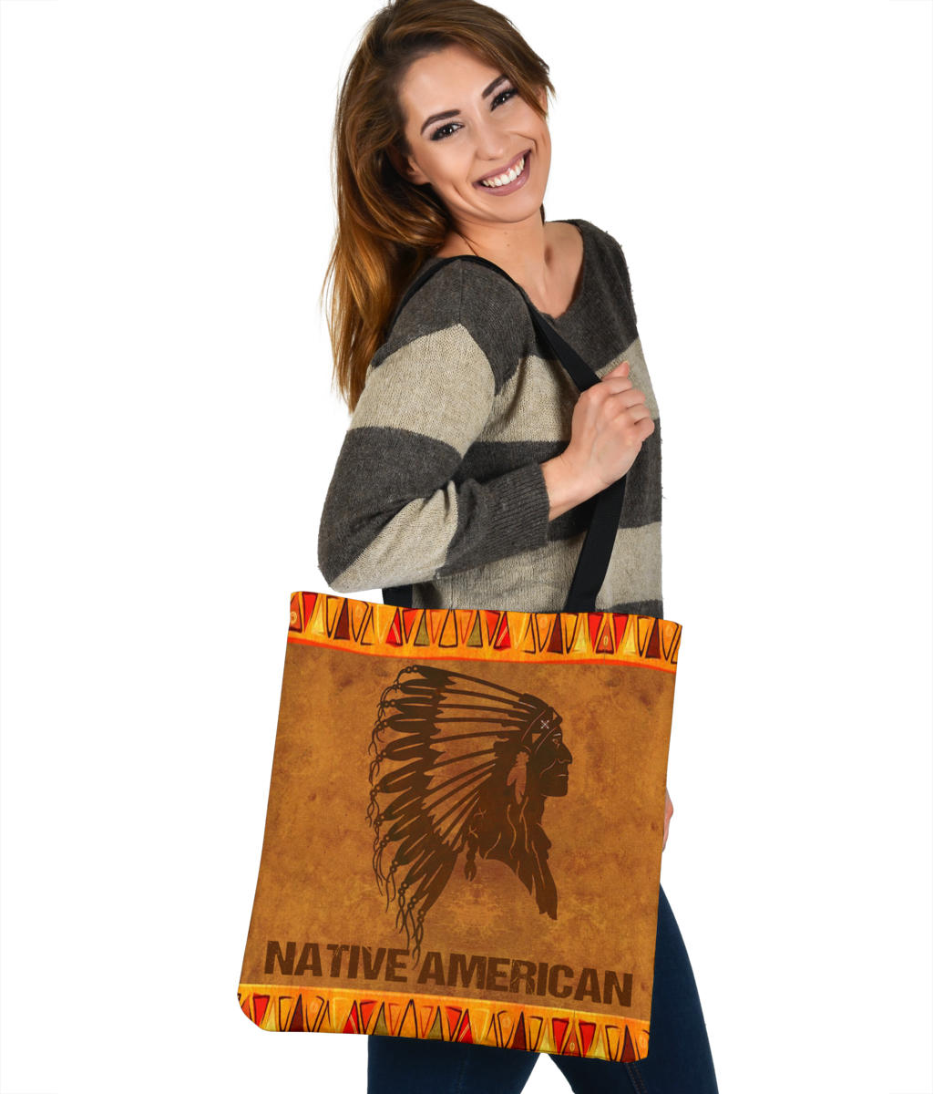 Brown tote with Native American text banner, black headdress image, orange tribal border and strap