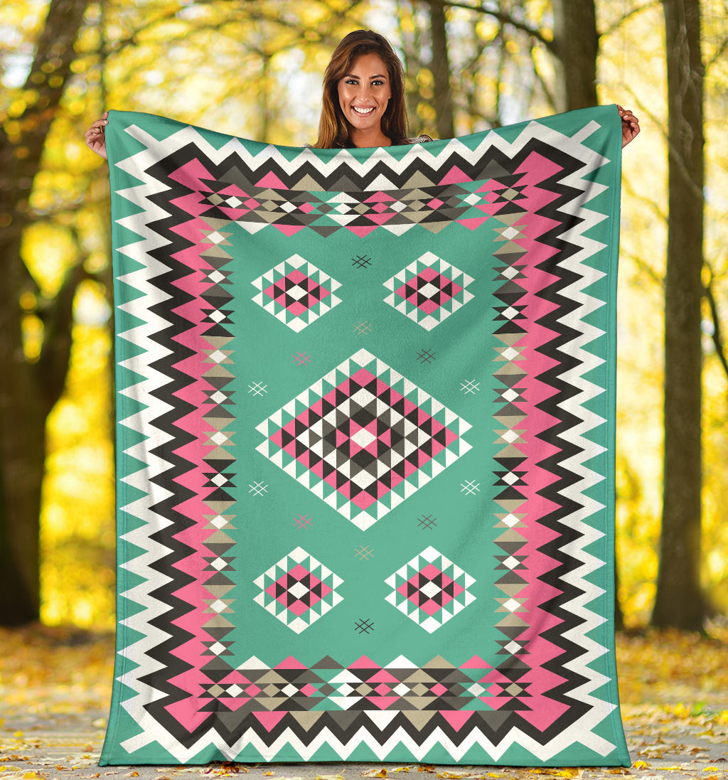 Turquoise geometric blanket with pink, black, and white diamond motifs and zigzag trim