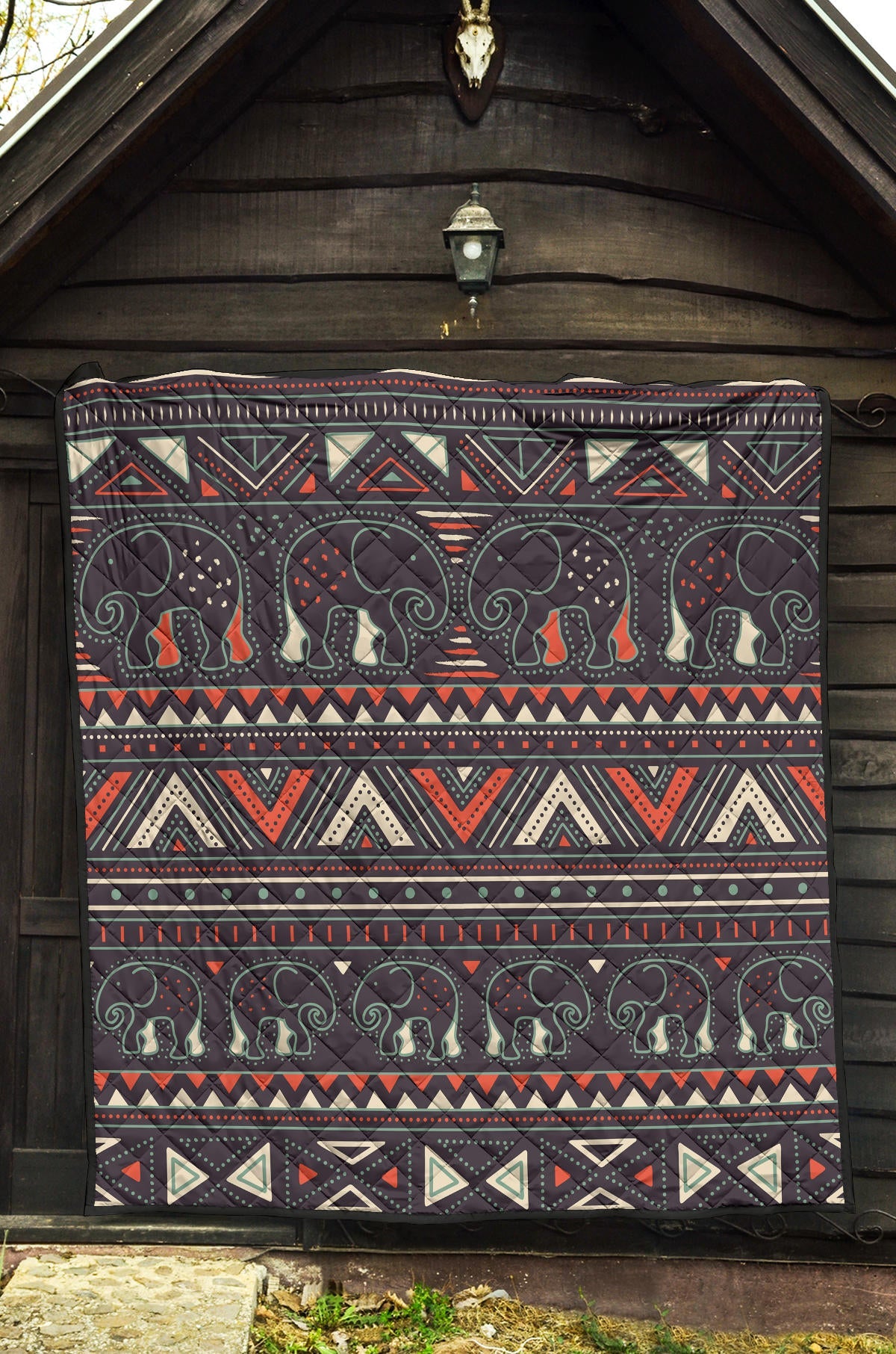 Native-style tribal elephant quilt hanging with dark base, red accents, and cream triangles