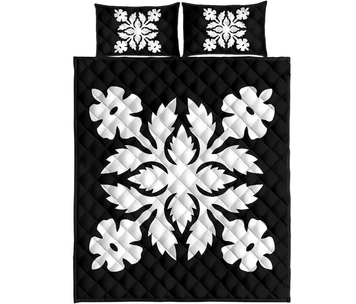 Flat lay of black quilt bed set with white floral medallion pattern and two pillows