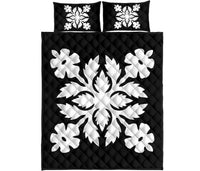 Flat lay of black quilt bed set with white floral medallion pattern and two pillows