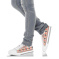 White low-top sneakers worn with jeans, Aztec pattern side panel and white laces