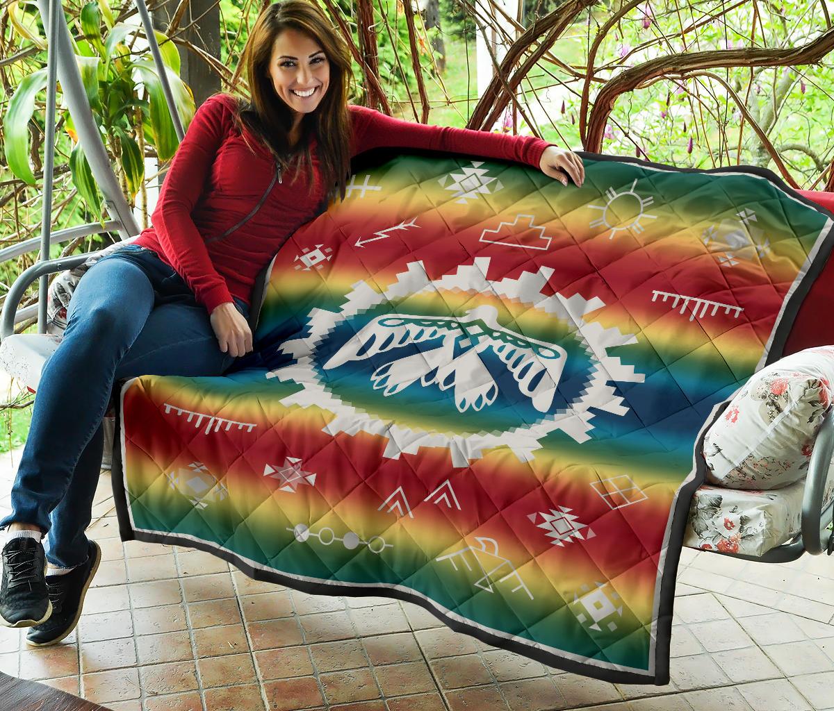 Rainbow quilt laid out with white thunderbird design and Native-style geometric borders