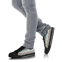 Low-top canvas sneakers on legs with light denim jeans; tribal print upper, black sole