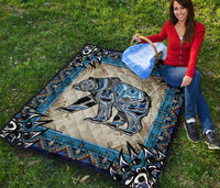 Bear symbol quilt spread flat: light tan center with blue/black bear and patterned edges
