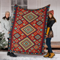 Geometric throw blanket held by two people, red teal and green diamonds with navy trim