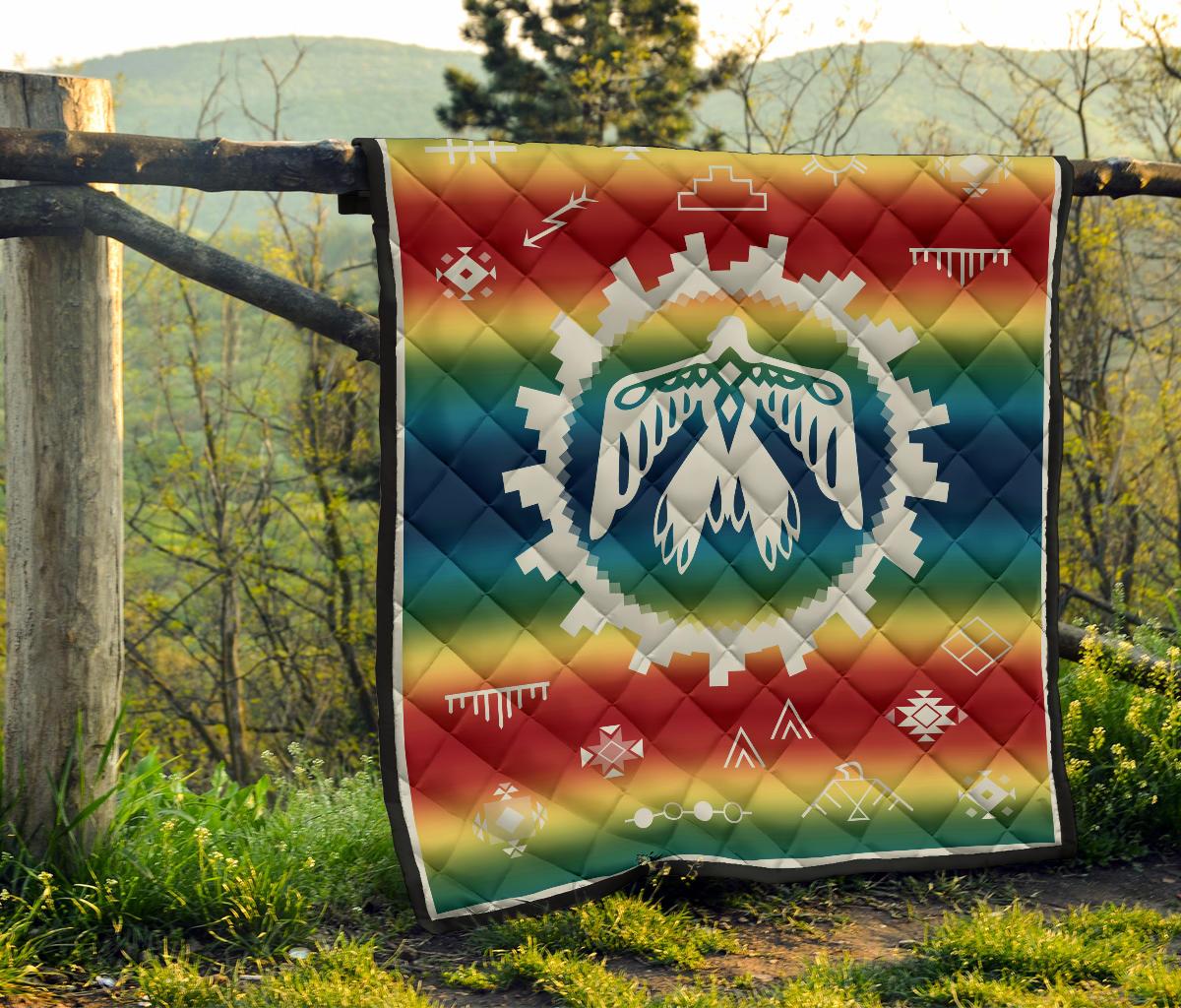 Rainbow Native quilt hanging with white thunderbird emblem and multicolor geometric motifs