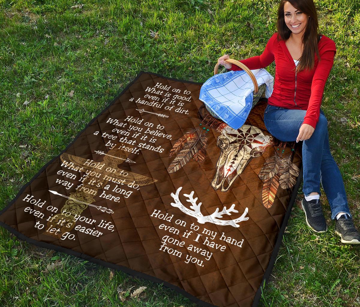 Brown quilt spread out outdoors with bison head graphic, feathers, and white sayings