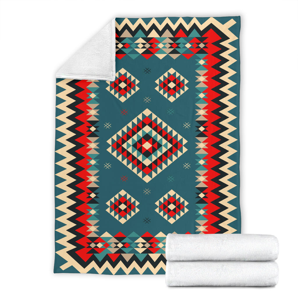 Teal geometric blanket with diamond and zigzag design, shown with rolled white blankets