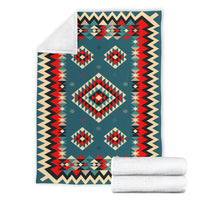 Teal geometric blanket with diamond and zigzag design, shown with rolled white blankets