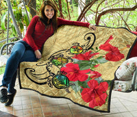Beige premium quilt draped over seating, featuring black turtles and red hibiscus flowers