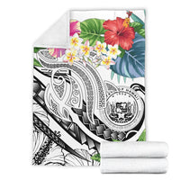 White Polynesian blanket folded with plumeria and hibiscus print; two rolled white blankets