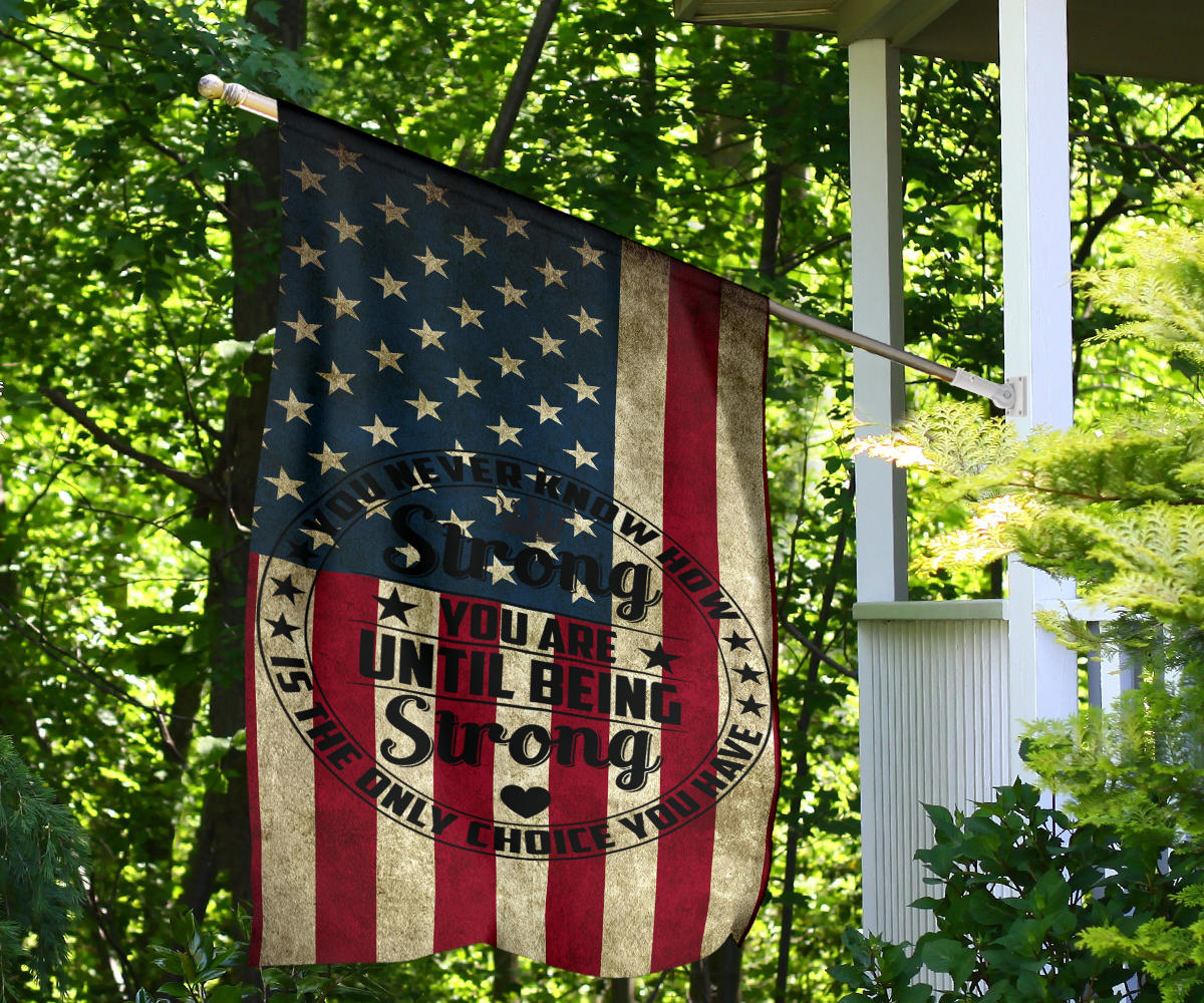 Patriotic house flag on porch post, star field and red/cream stripes with “You are… Strong”