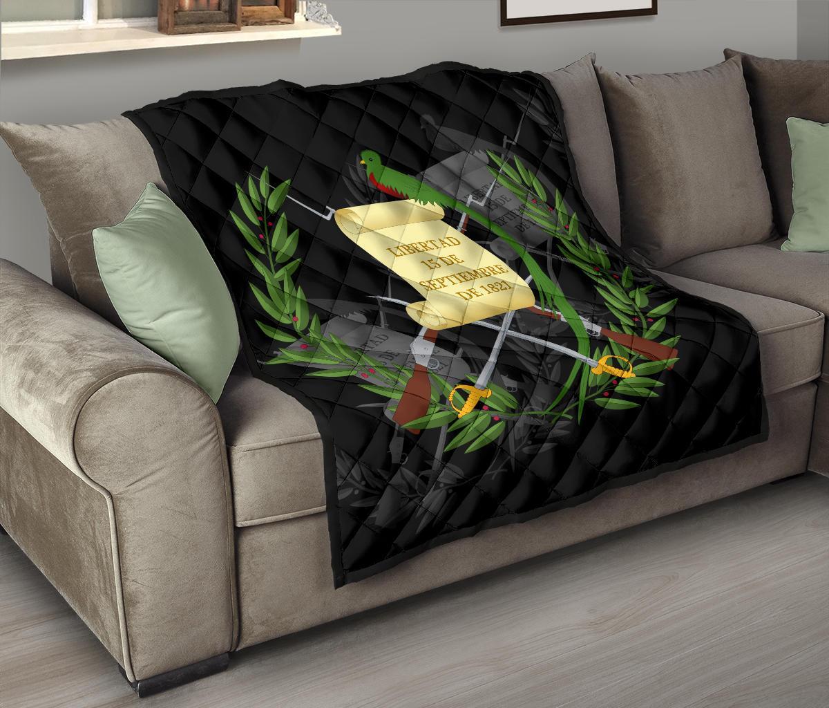 Black quilt draped on sofa, featuring Guatemala emblem banner and parrot with laurel