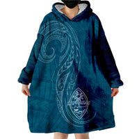 Dark teal wearable blanket hoodie with hood, oversized front pocket, and crest graphic
